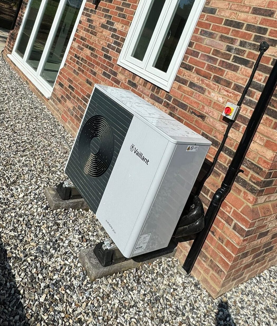 An air source heat pump installed by Neater Heat, mounted neatly on an external wall of a residential property. The sleek, modern unit is positioned on a stable base with secure piping and wiring, showcasing a clean and professional installation. Surrounded by well-maintained landscaping, the setup reflects Neater Heat's attention to detail and commitment to high-quality renewable energy solutions