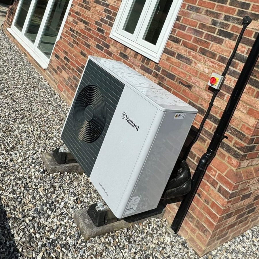 An air source heat pump installed by Neater Heat, mounted neatly on an external wall of a residential property. The sleek, modern unit is positioned on a stable base with secure piping and wiring, showcasing a clean and professional installation. Surrounded by well-maintained landscaping, the setup reflects Neater Heat's attention to detail and commitment to high-quality renewable energy solutions